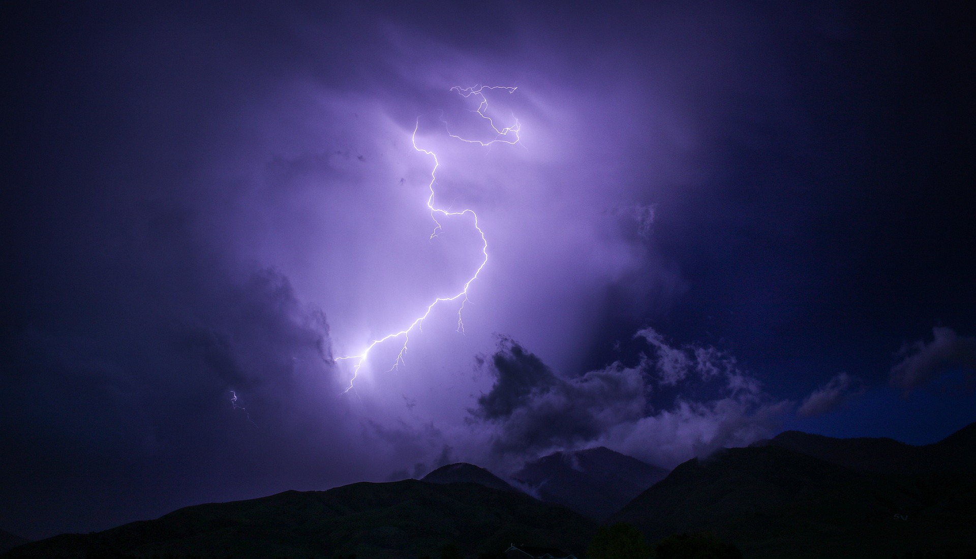 A lightning bolt breaks darkened skies over black hills